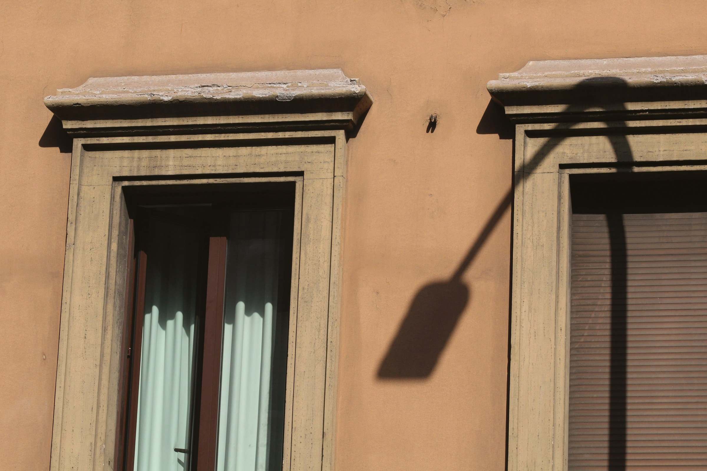 Stone window frames set into warm ochre plaster, a lamp casting a long shadow
