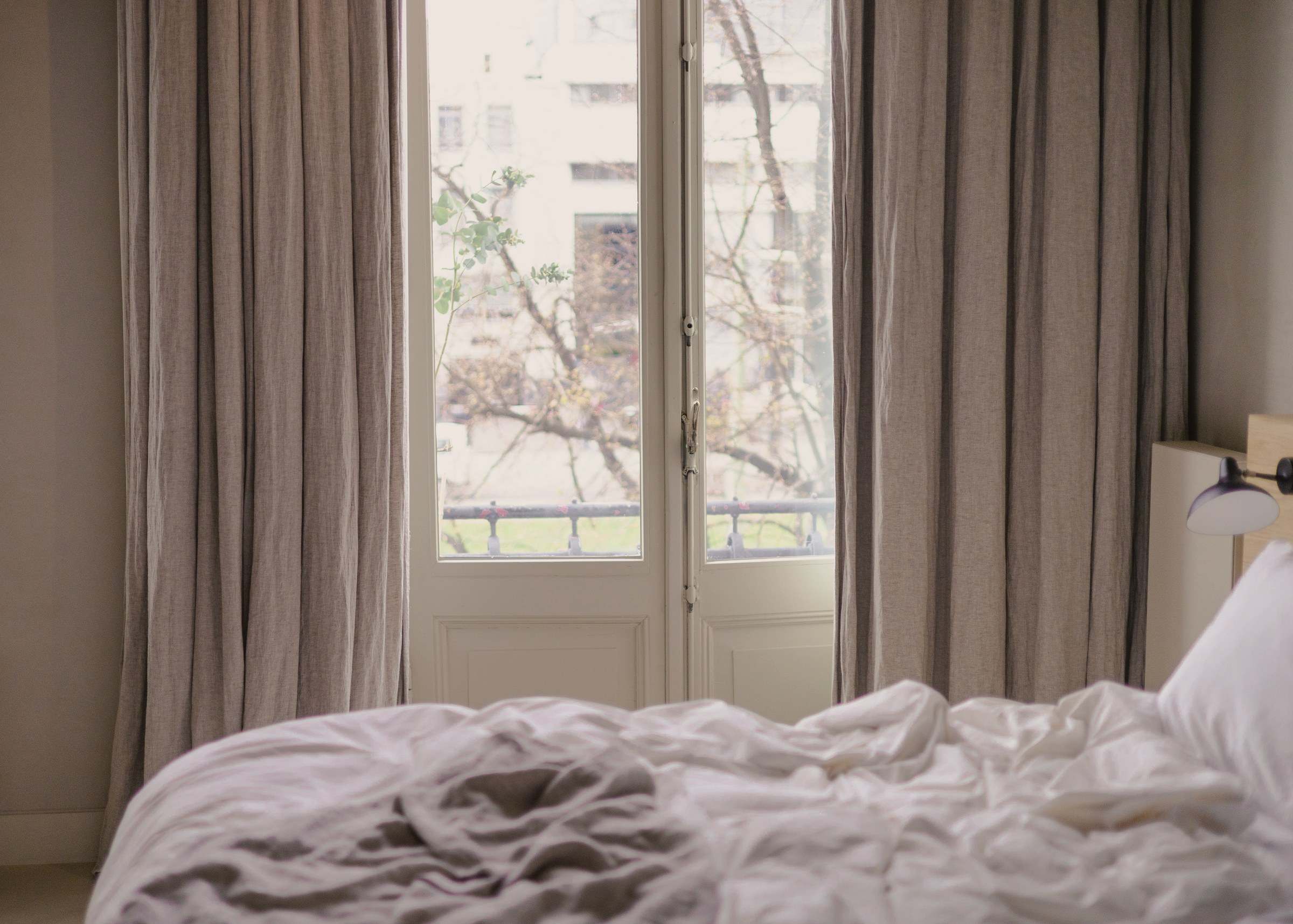 Linen curtains and an open window above a bed